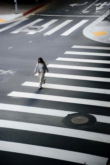 Woman in casual clothing crosses a zebra crossing in an urban setting on a sunny day, captured from a high angle view.
