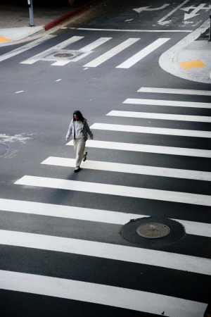 Woman in casual clothing crosses a zebra crossing in an urban setting on a sunny day, captured from a high angle view.