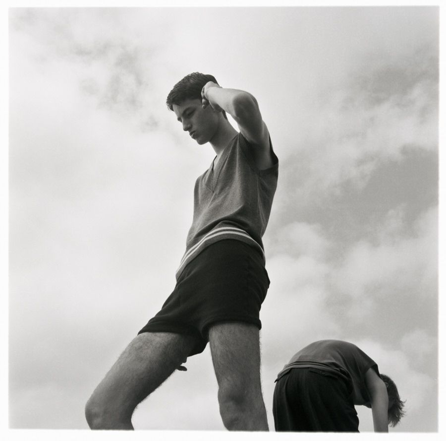 Two young adult males pose outside against a cloudy sky, one standing, one bent over, in a high-contrast black-and-white outdoor photograph.