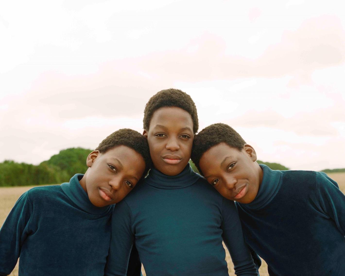 Portrait of three African adolescent boys in blue turtleneck shirts, close-up shot outdoors with soft, diffused lighting and a neutral background.