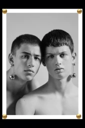 Portrait of two young male models wearing metallic drop sphere earrings styled by Adam Winder against a grey background.