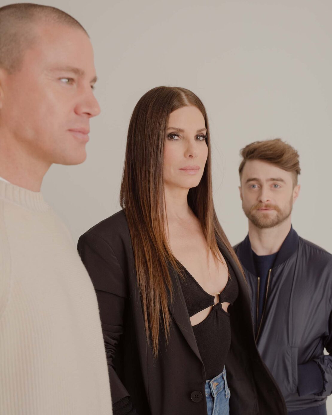 Promotional photo of Channing Tatum, Sandra Bullock, and Daniel Radcliffe in front of a plain background. Radcliffe wears a bomber jacket.