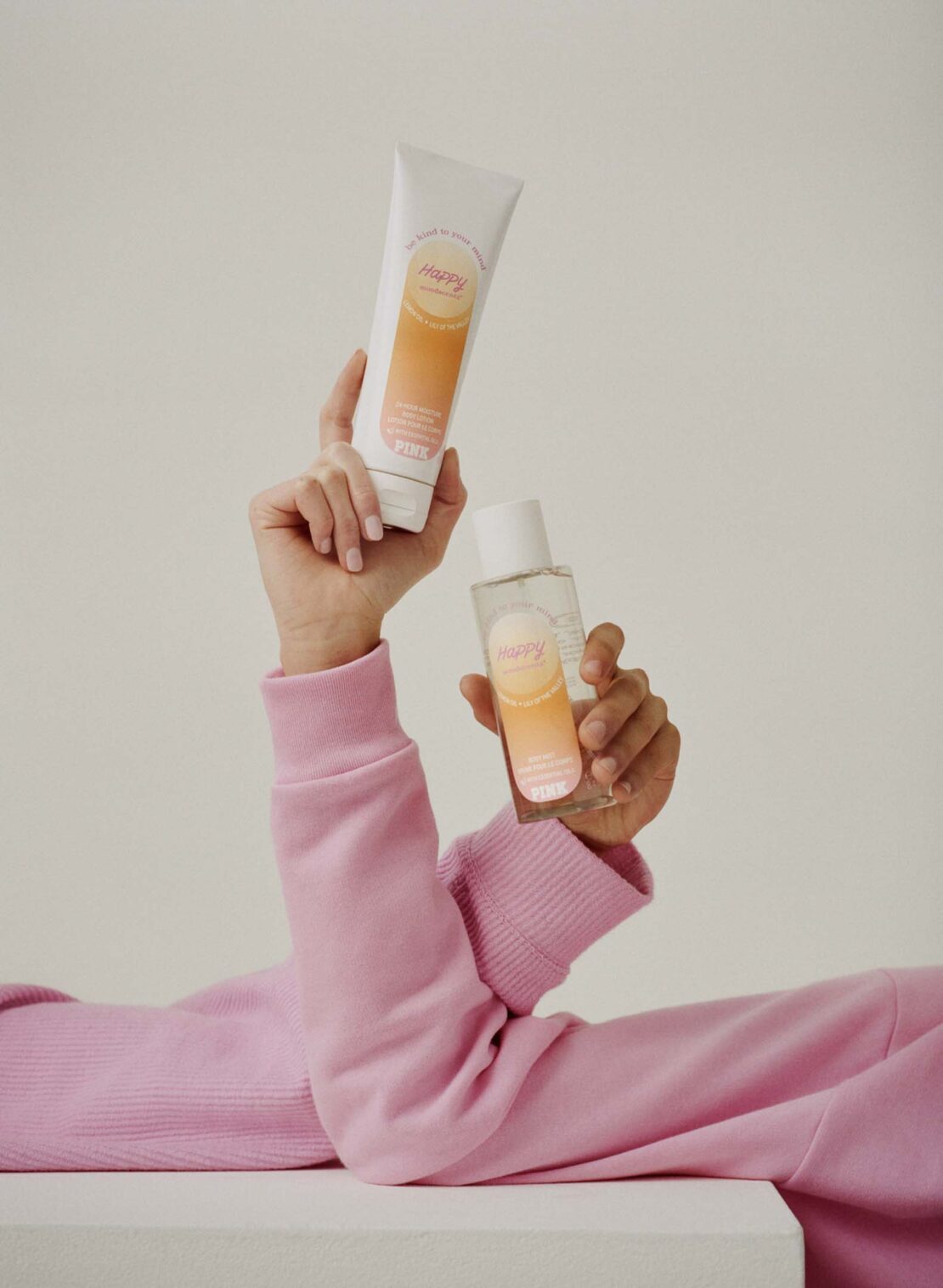 Person holds a tube and a bottle of skincare product with gradient orange labels in a studio setting against a neutral background.
