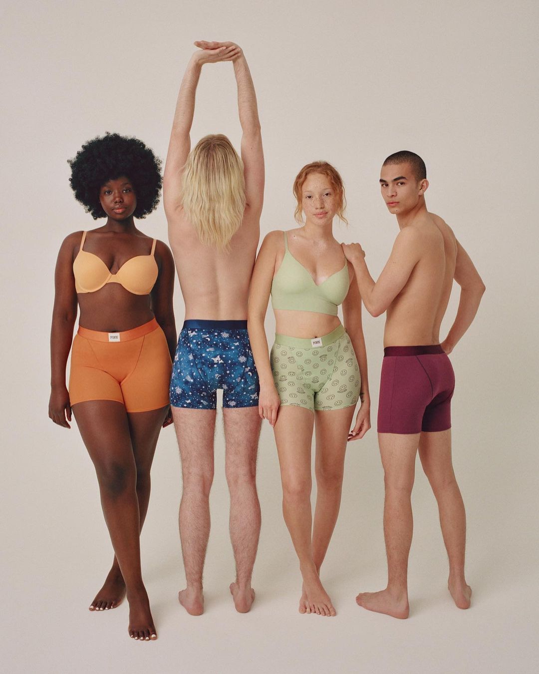 Four diverse adults pose in underwear sets against a neutral backdrop, showcasing various skin tones and body types in a studio setting.