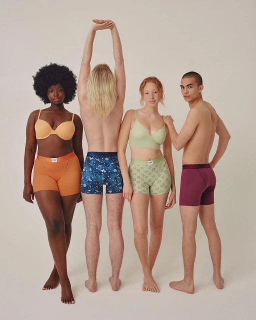 Four diverse adults pose in underwear sets against a neutral backdrop, showcasing various skin tones and body types in a studio setting.
