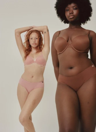 Two women of different skin tones pose in matching bras and underwear in a studio shot against a neutral background.