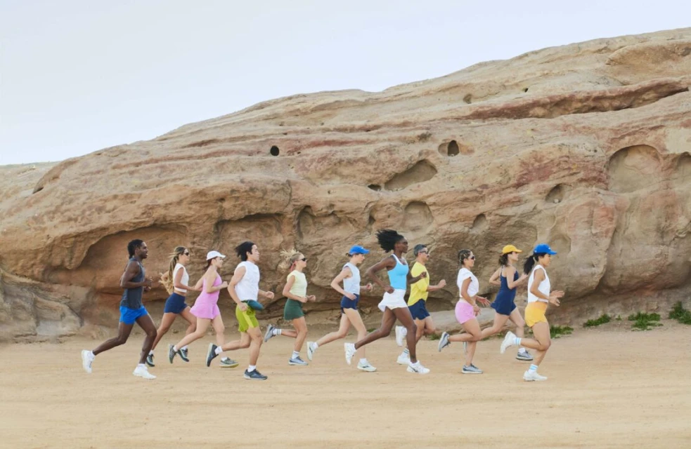 Group of diverse adults running outdoors on a sandy path with a large rock formation in the background on a sunny day, athletic wear.