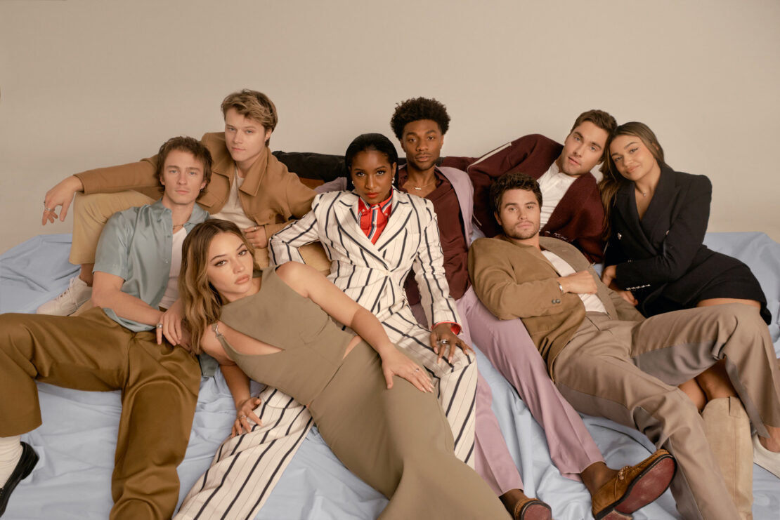Group studio portrait of eight young adult diverse people, posing, wearing fashionable outfits in earth tones, horizontal orientation.