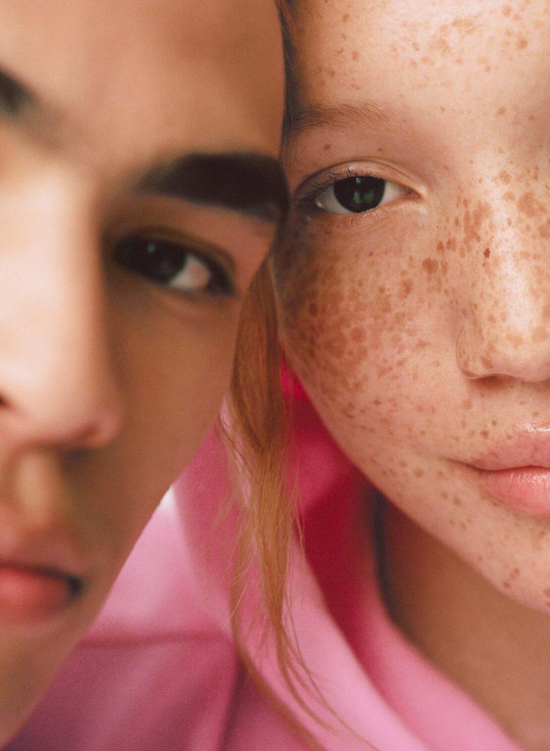 Close-up studio shot featuring two faces: a fair-skinned young adult with freckles and another with warm skin tone, both next to each other.