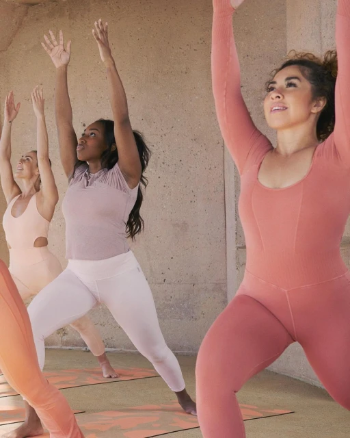 Three women in sportswear doing yoga outdoors against a concrete wall with raised arms. Fitness and healthy lifestyle concept. 