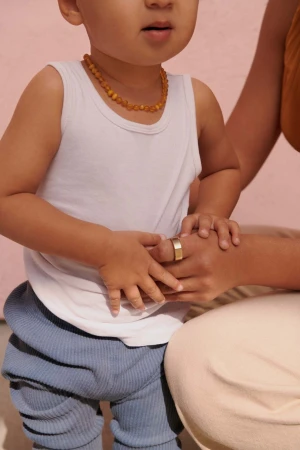Close-up portrait of a toddler wearing a white tank top and blue textured pants standing next to an adult holding hands.