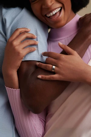 Close-up portrait of two people embracing warmly with one wearing a light blue textured shirt and the other wearing a pink top and silver ring