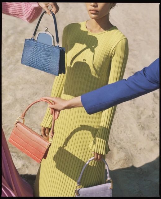 Fashion editorial featuring a model in yellow dress surrounded by three handbags held by other people in colorful blazers.