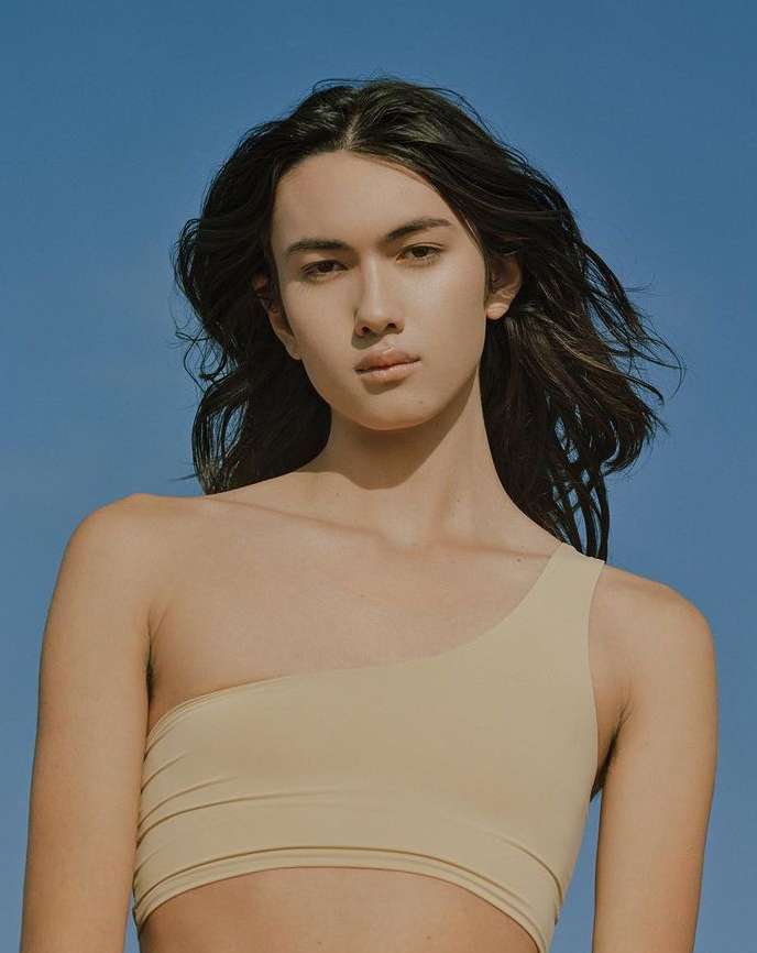 Portrait of a long-haired model wearing a beige one-shoulder top against a clear blue sky by Amy Harrity.