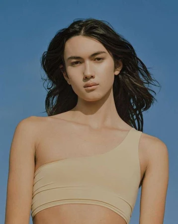 Portrait of a long-haired model wearing a beige one-shoulder top against a clear blue sky by Amy Harrity.