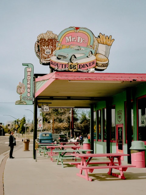 Retro Route 66 diner exterior with vintage signage and classic cars; man in suit standing outside, vintage atmosphere, roadside architecture.