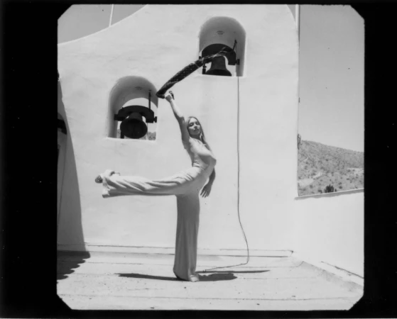 Monochrome portrait of a woman posing with an outstretched leg on a rooftop against a white bell tower by Amy Harrity