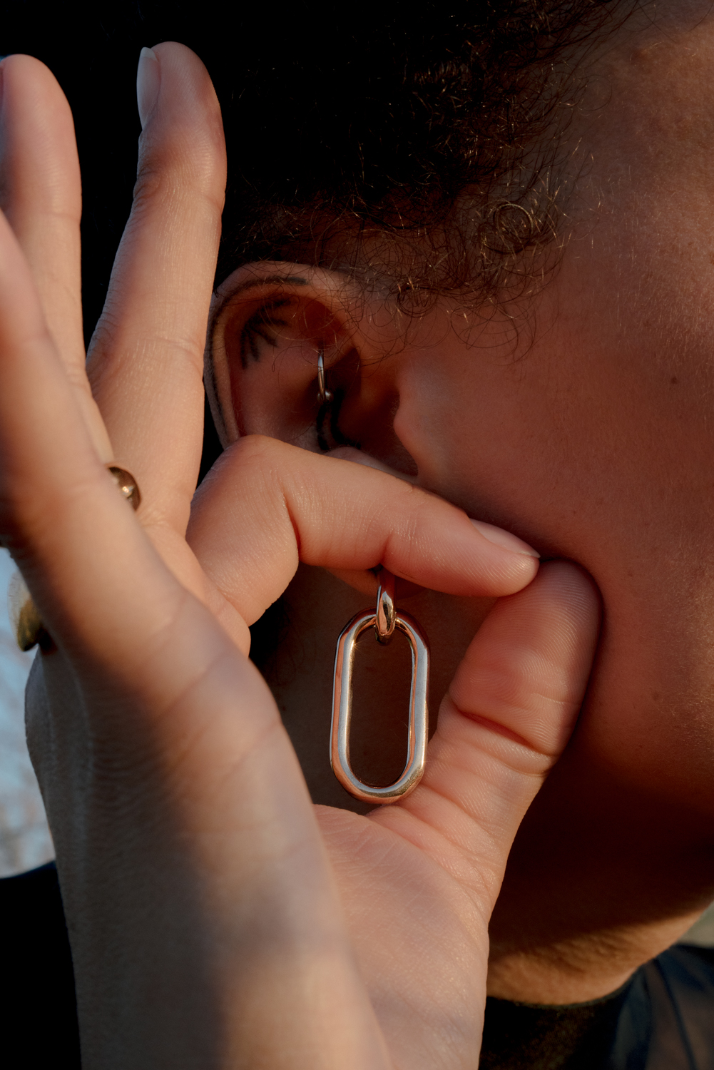 Close-up of a person's ear adorned with a hoop earring, fingers holding a gold geometric earring, and hair framing the shot.