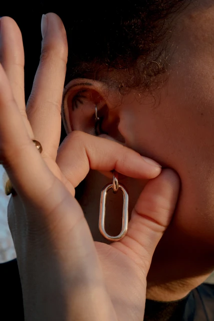 Close-up of a person's ear adorned with a hoop earring, fingers holding a gold geometric earring, and hair framing the shot.