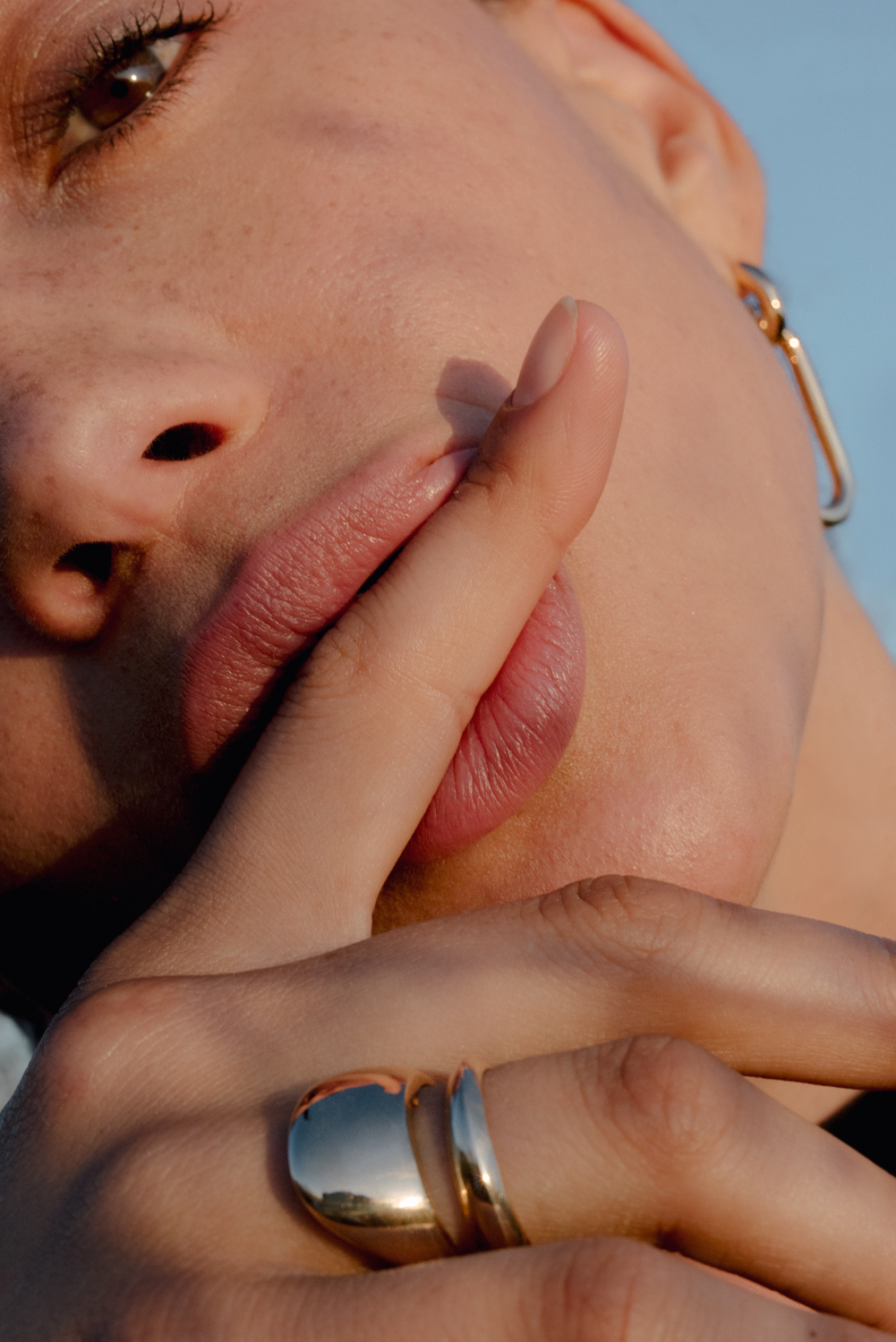 Close-up of a woman with an earring holding a finger to her lips, wearing rings, and the soft natural lighting.