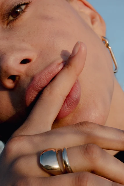 Close-up of a woman with an earring holding a finger to her lips, wearing rings, and the soft natural lighting.