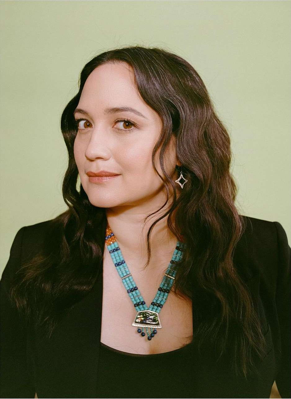 Portrait of a woman wearing a turquoise beaded necklace and black jacket against a light green background.