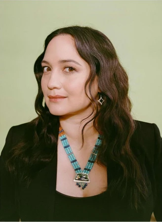 Portrait of a woman wearing a turquoise beaded necklace and black jacket against a light green background.