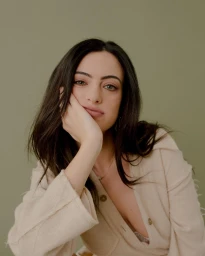 Portrait of a woman with dark hair leaning her head on her hand against an olive green background