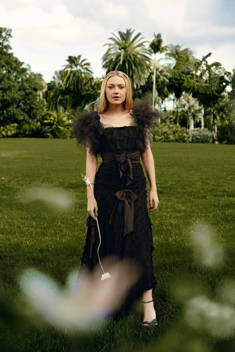 Portrait of a blonde woman wearing a black tulle gown standing on a green lawn by Amy Harrity