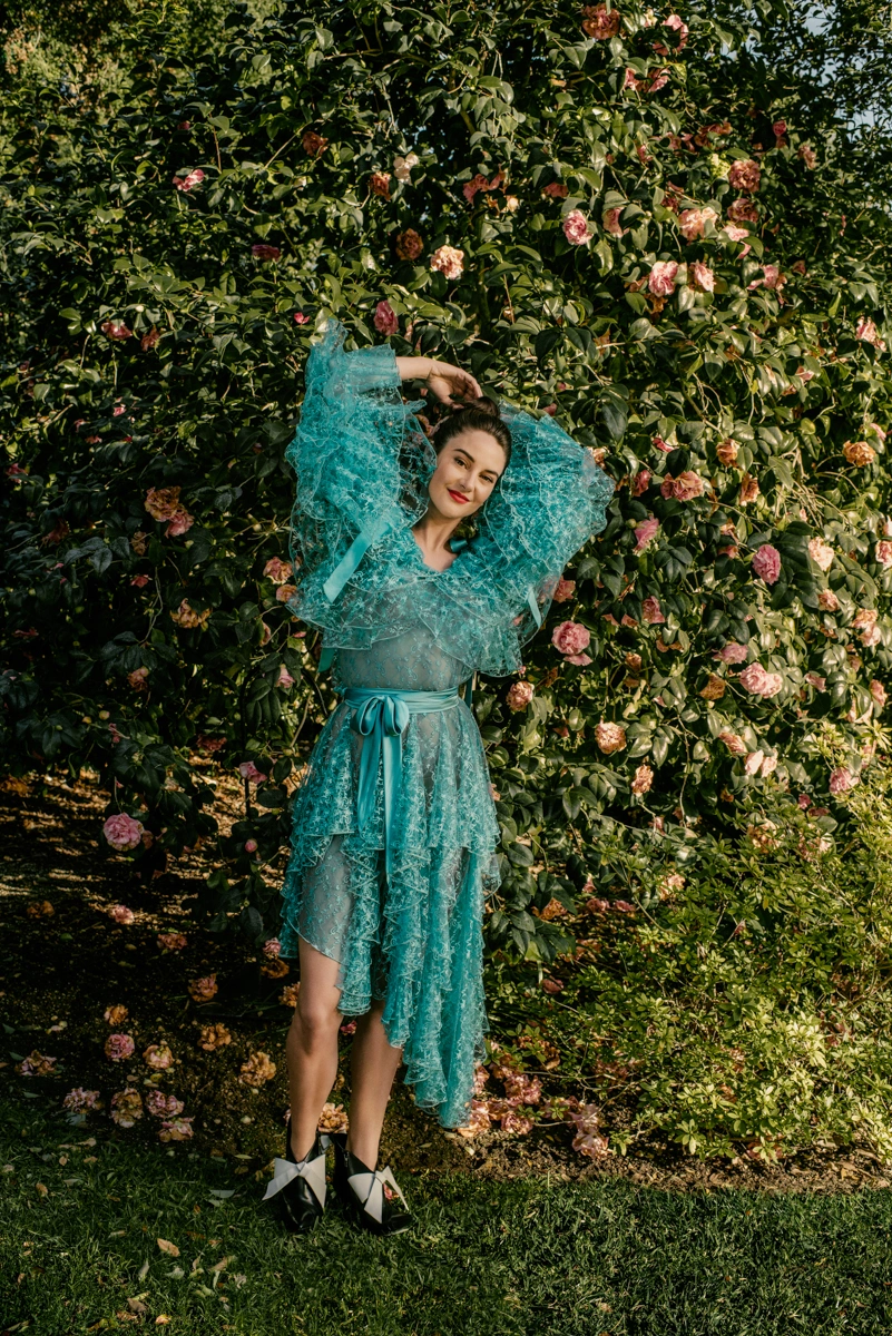Woman in a ruffled turquoise tulle dress posing in front of a dense flowering rose bush in Los Angeles by photographer Amy Harrity.