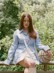 Woman with long brown hair seated outdoors wearing a striped blue shirt and holding a basketball, photographed by Amy Harrity.