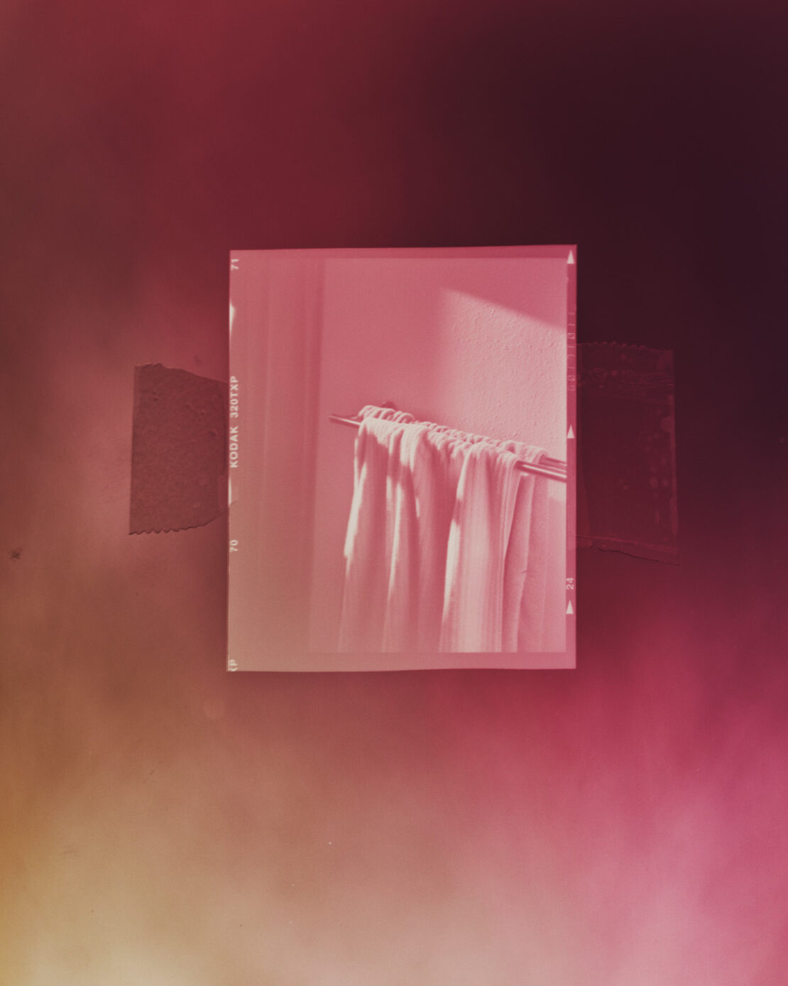 Still life photo of white towels hanging on a metal rod against a textured wall, captured within a vintage film border.