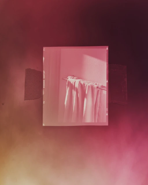 Still life photo of white towels hanging on a metal rod against a textured wall, captured within a vintage film border.