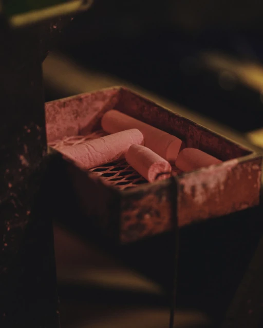 Close-up of pink chalk sticks in a rusted metal tray with a grate bottom, set against a blurred, dark background, moody lighting.