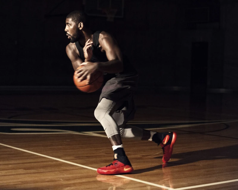 Basketball player in action on court, dribbling a basketball while wearing athletic shoes, grey leggings and a black top, in dynamic motion.