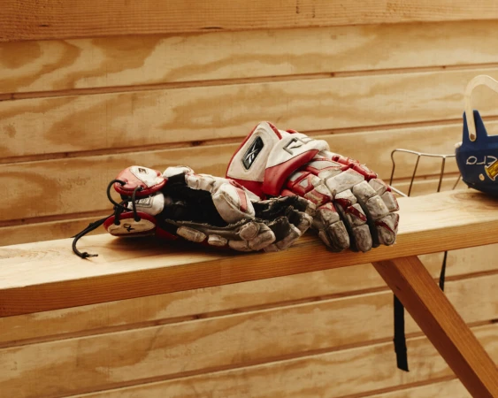 Worn red and white hockey gloves resting on a wooden bench against a panelled wall