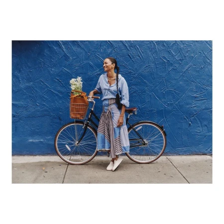 Woman leaning on a bicycle with a basket of white flowers against a textured blue wall by Clayton Cotterell