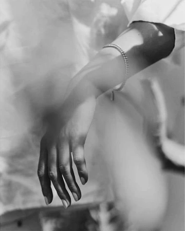 Close-up monochrome portrait of a person's hand and wrist wearing a delicate silver chain bracelet.