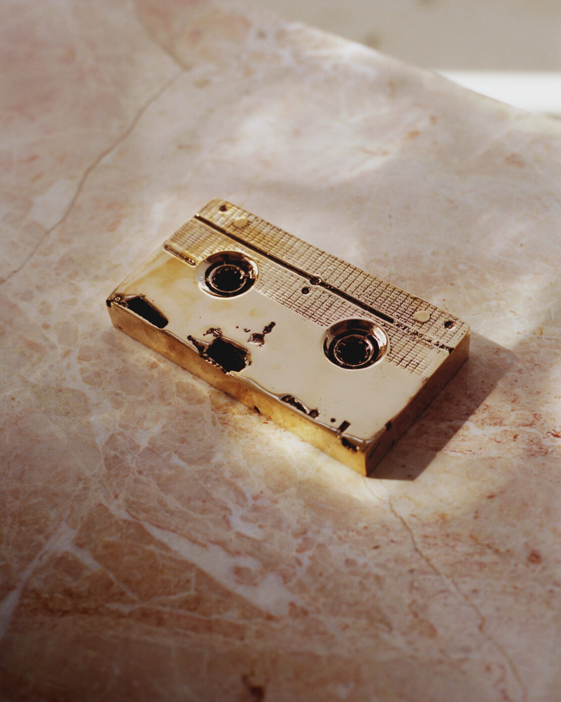Close-up of a gold-colored audio cassette tape on a marble surface, illuminated by a soft, diffused light.