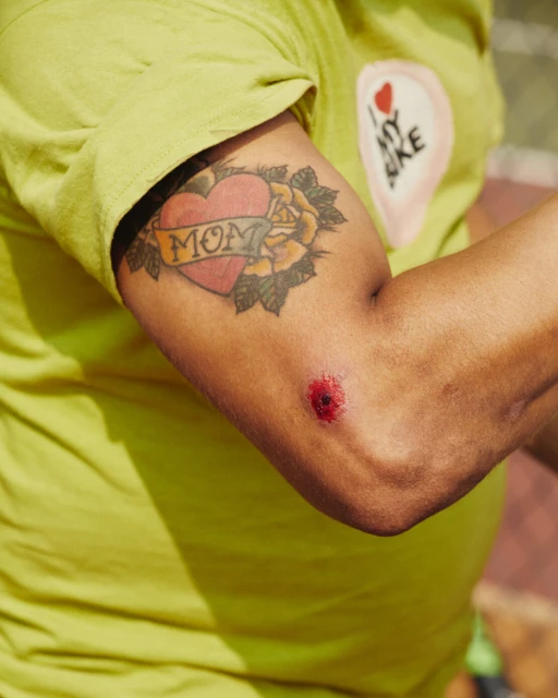 Close-up of an arm with a tattoo of a heart, rose and the word 'Mom', alongside a 'I love my bike' graphic on a green t-shirt.