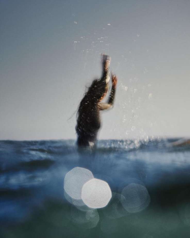 Surfer diving into ocean waves with motion blur and water spray, captured by Clayton Cotterell.