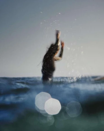 Surfer diving into ocean waves with motion blur and water spray, captured by Clayton Cotterell.