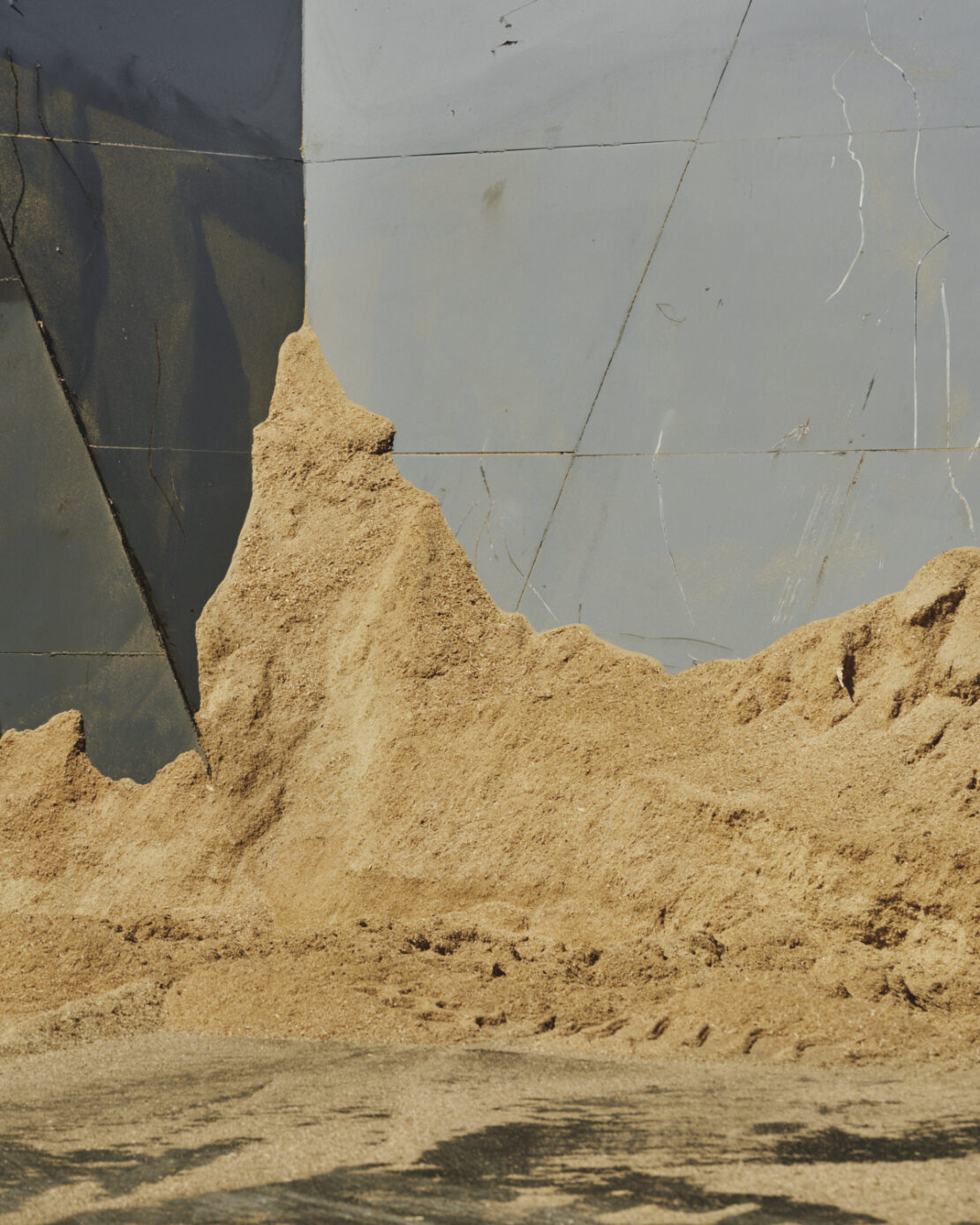 Close-up shot of a pile of sawdust or wood shavings against a grey surface with dark shadows, showcasing industrial textures and patterns.
