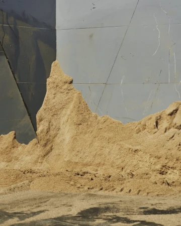 Close-up shot of a pile of sawdust or wood shavings against a grey surface with dark shadows, showcasing industrial textures and patterns.