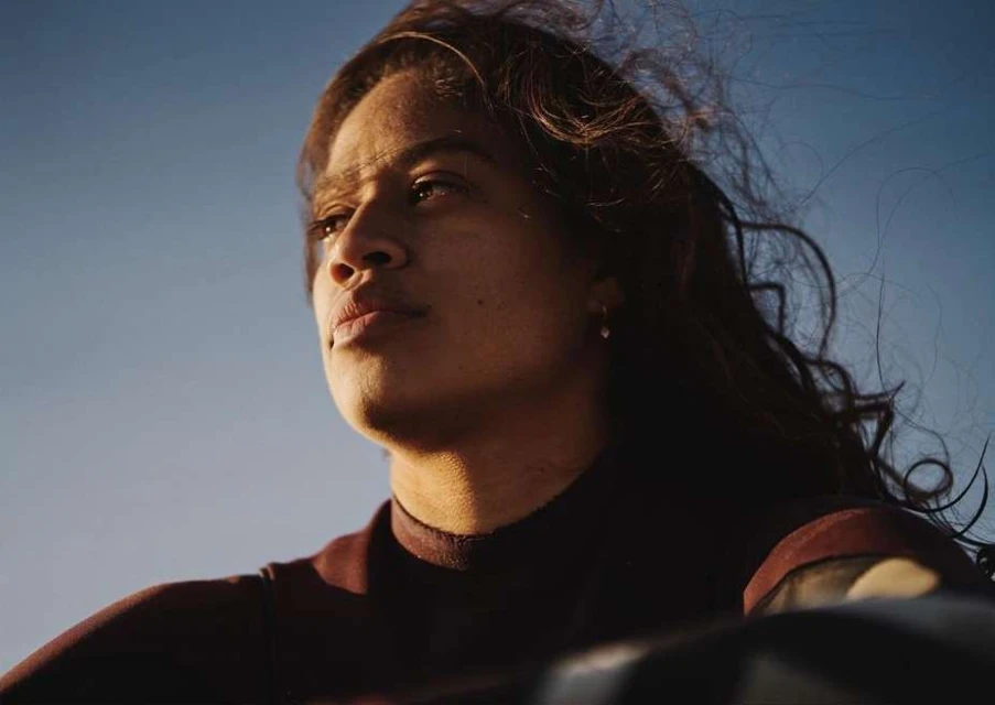 Close up portrait of a serene adult woman with long hair against a clear blue sky during golden hour, looking off into the distance.