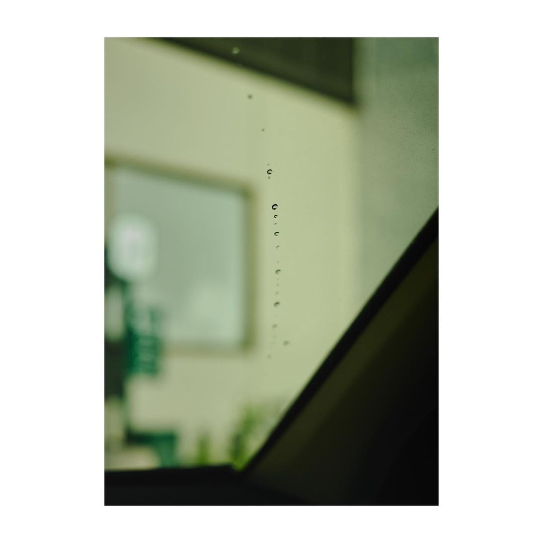 Raindrops on a window, with a blurry view of an indoor office space, seen through the glass, casting a moody and introspective atmosphere.