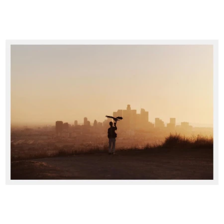 Person holding a bird silhouette against the Los Angeles skyline at sunset, creating a peaceful, golden-hour urban nature scene.