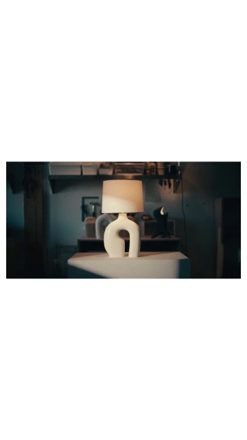 Contemporary table lamp with a white curved base and a lampshade on a table in a dimly lit room showcasing interior design.
