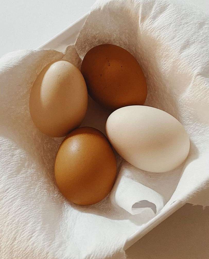 Overhead shot of four chicken eggs in a variety of brown and white hues, arranged on a white textured cloth in soft natural light.