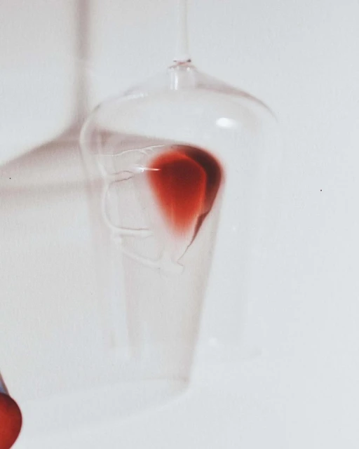 A clear glass goblet holds a red liquid against a pale background, illuminated by an external light source casting soft shadows.